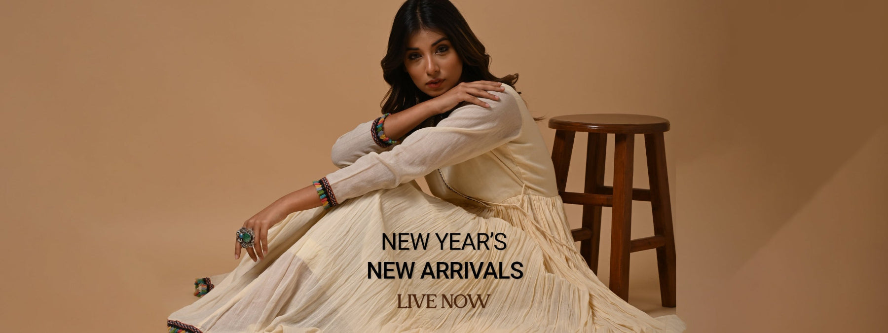 Woman in a cream dress sitting on a stool with 'New Year's New Arrivals' text on a beige background